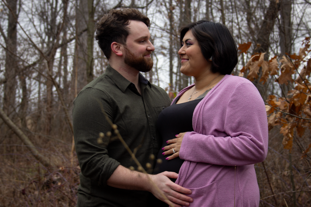 A couple shares an intimate moment during their maternity shoot in a fall forest setting.