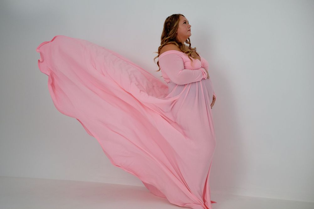 Flowing pink maternity gown creates dramatic movement in studio setting.