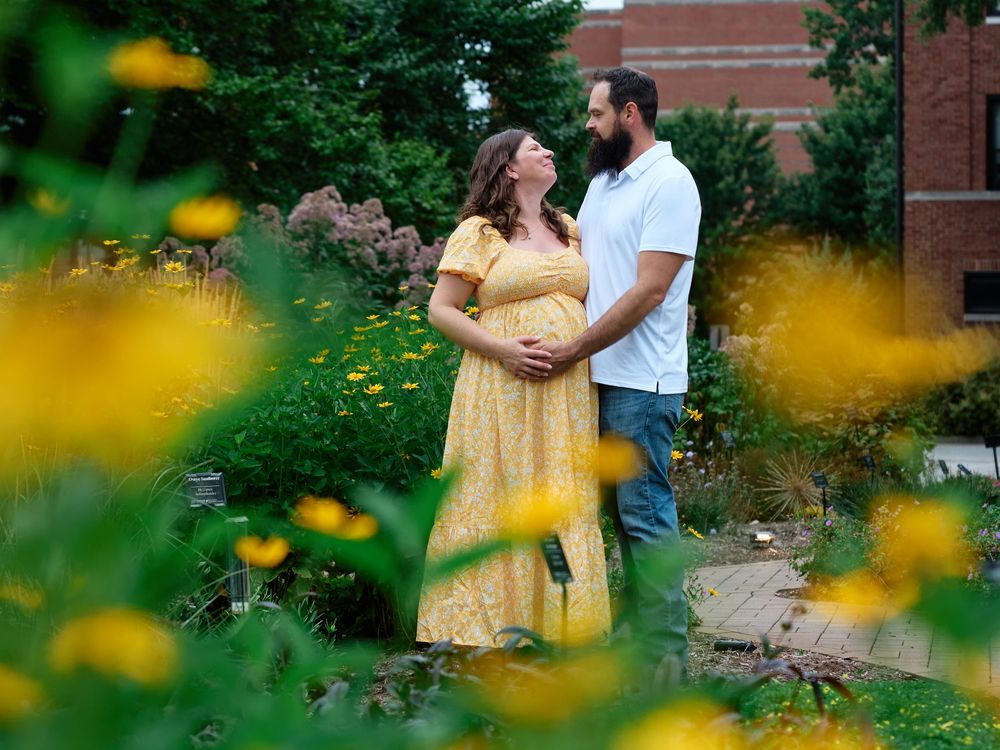 Pregnant couple embracing in a garden surrounded by yellow flowers during a maternity photo session.