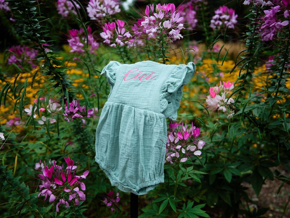 Light blue baby romper displayed among vibrant pink and purple wildflowers in a lush garden setting.