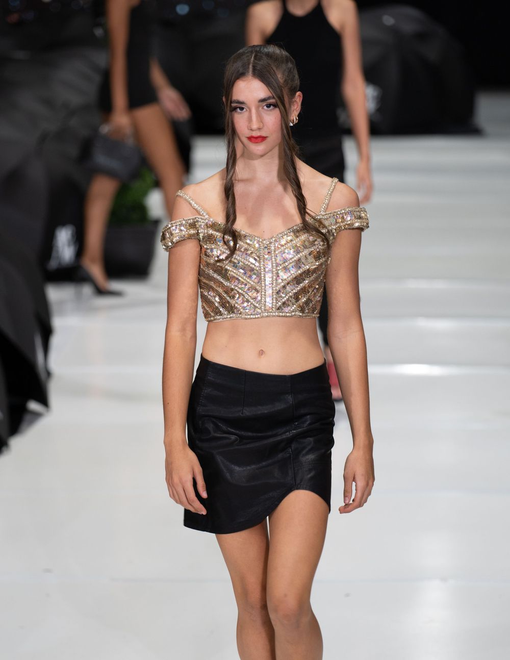 Gold sequined crop top paired with black mini skirt on fashion catwalk.