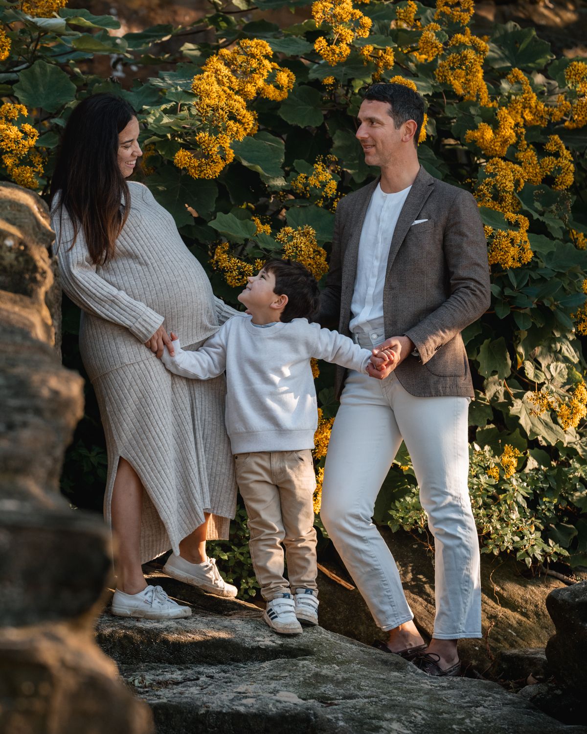 Pregnant mom, dad, and sons joyful moment looking at each other among flowers during a family photoshoot in Sydney