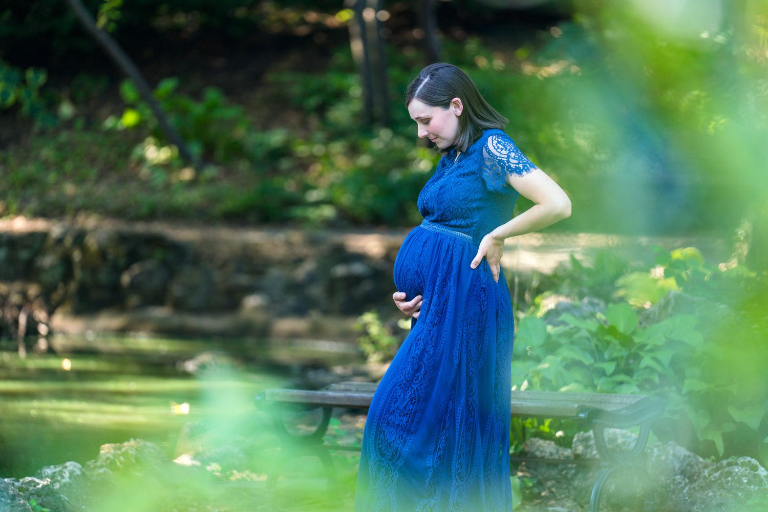 Maternity photo of woman in flowing blue dress by a stream.