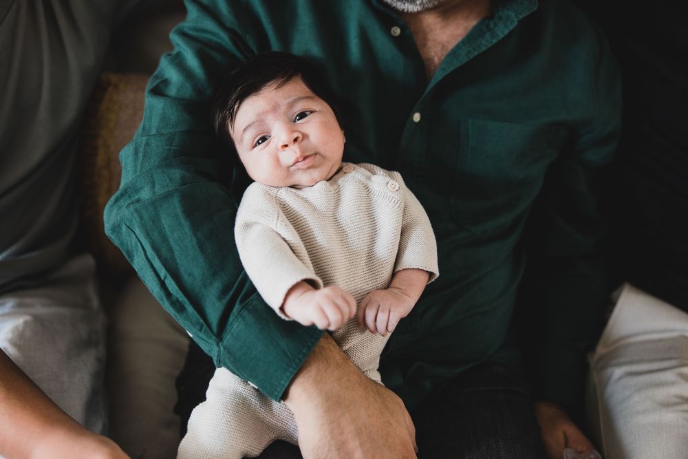 Baby lies peacefully in bed while wearing white onesie with dark teal blanket in background.