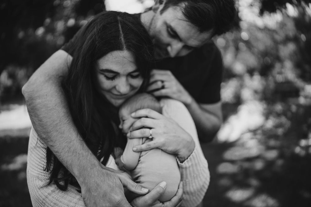 Black and white photos of a playful parent lovingly bonding with an infant in different candid moments and poses.
