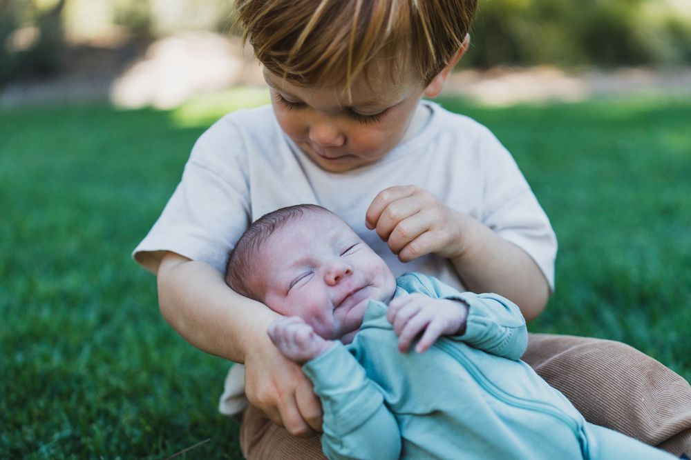 A series of outdoor photos showing tender moments between a parent and a baby in a light blue outfit on green grass.