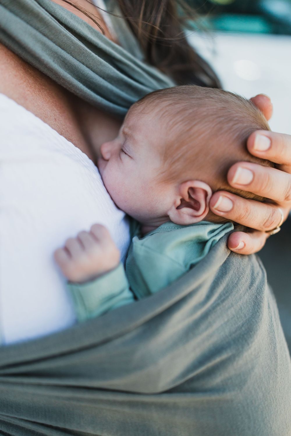 A montage of close-up shots showing a nursing infant feeding in a soft gray baby carrier.