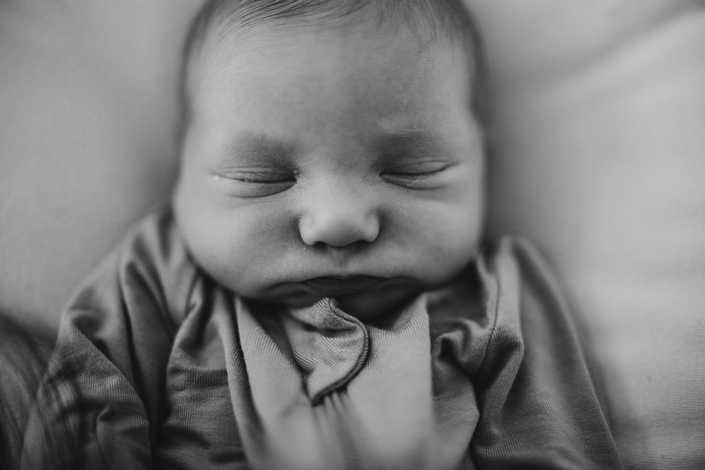 A peaceful sleeping newborn baby wearing a grey outfit in black and white photography.
