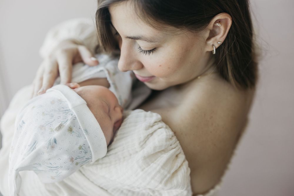 Tender moment between caregiver and newborn wrapped in white.