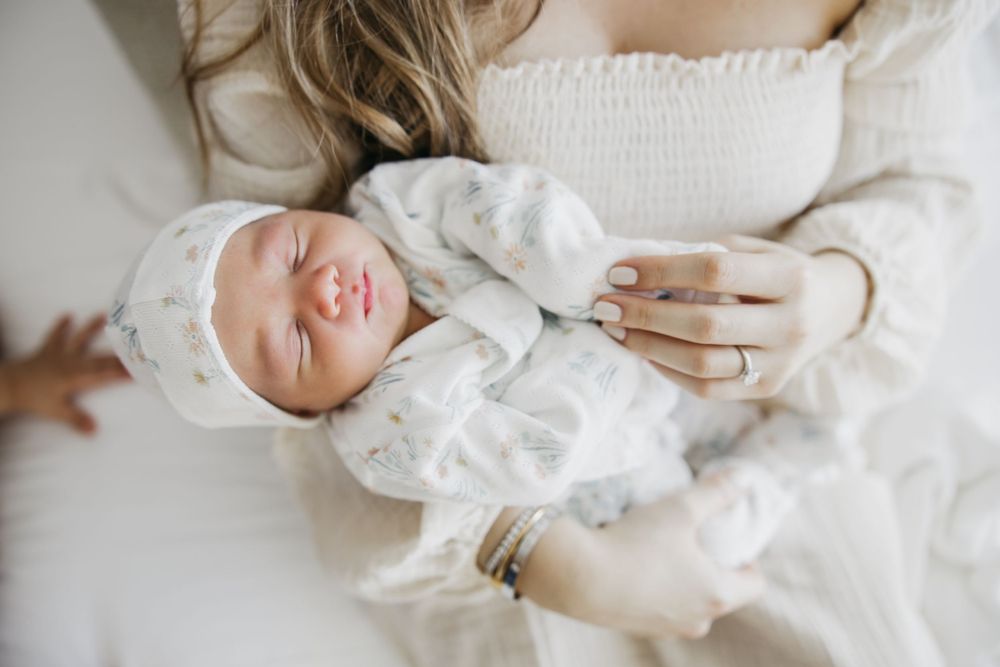 Sleeping newborn in white outfit rests peacefully on soft bedding.