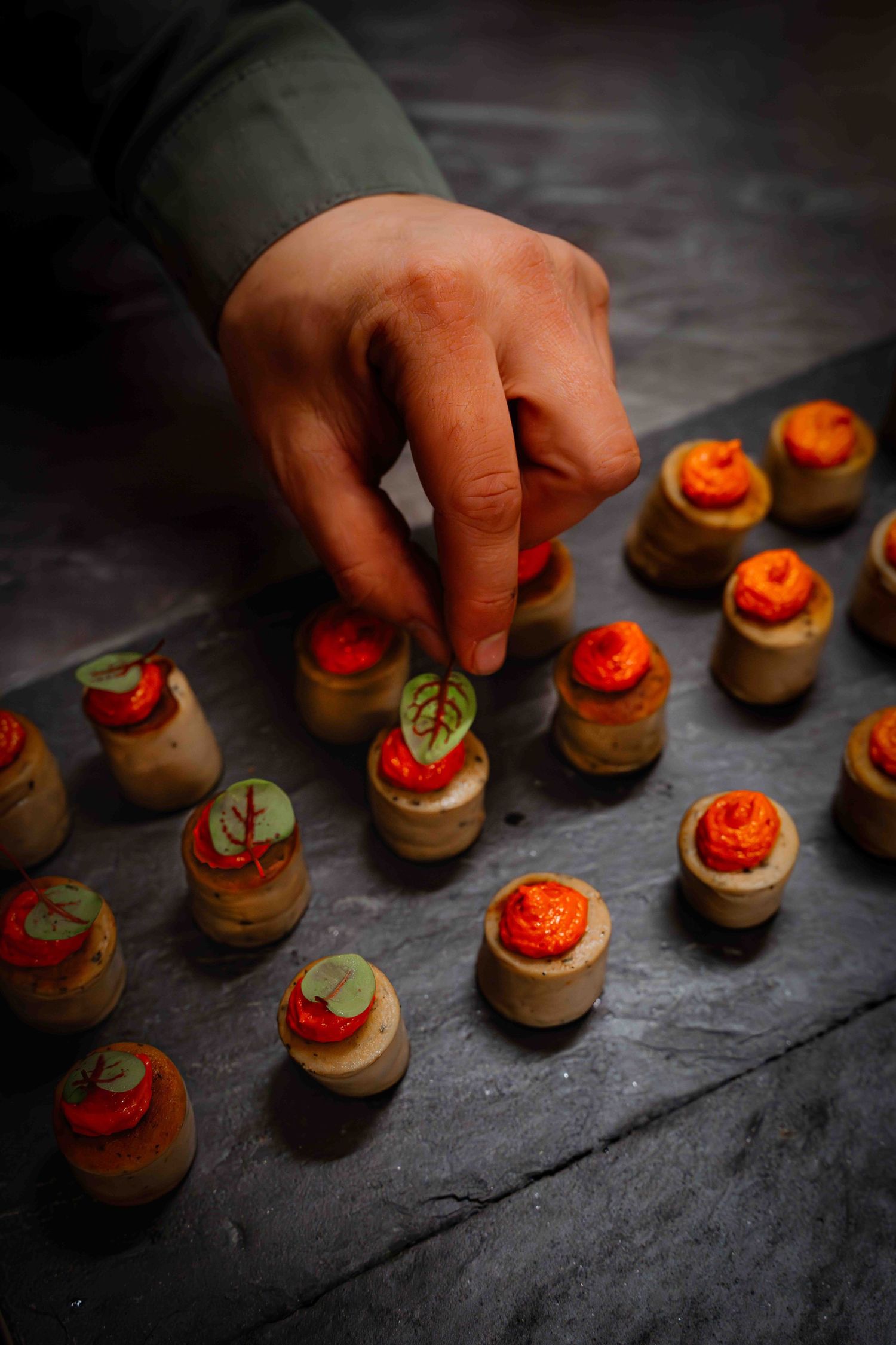 Hand placing delicate red-topped canapes on a dark stone surface.