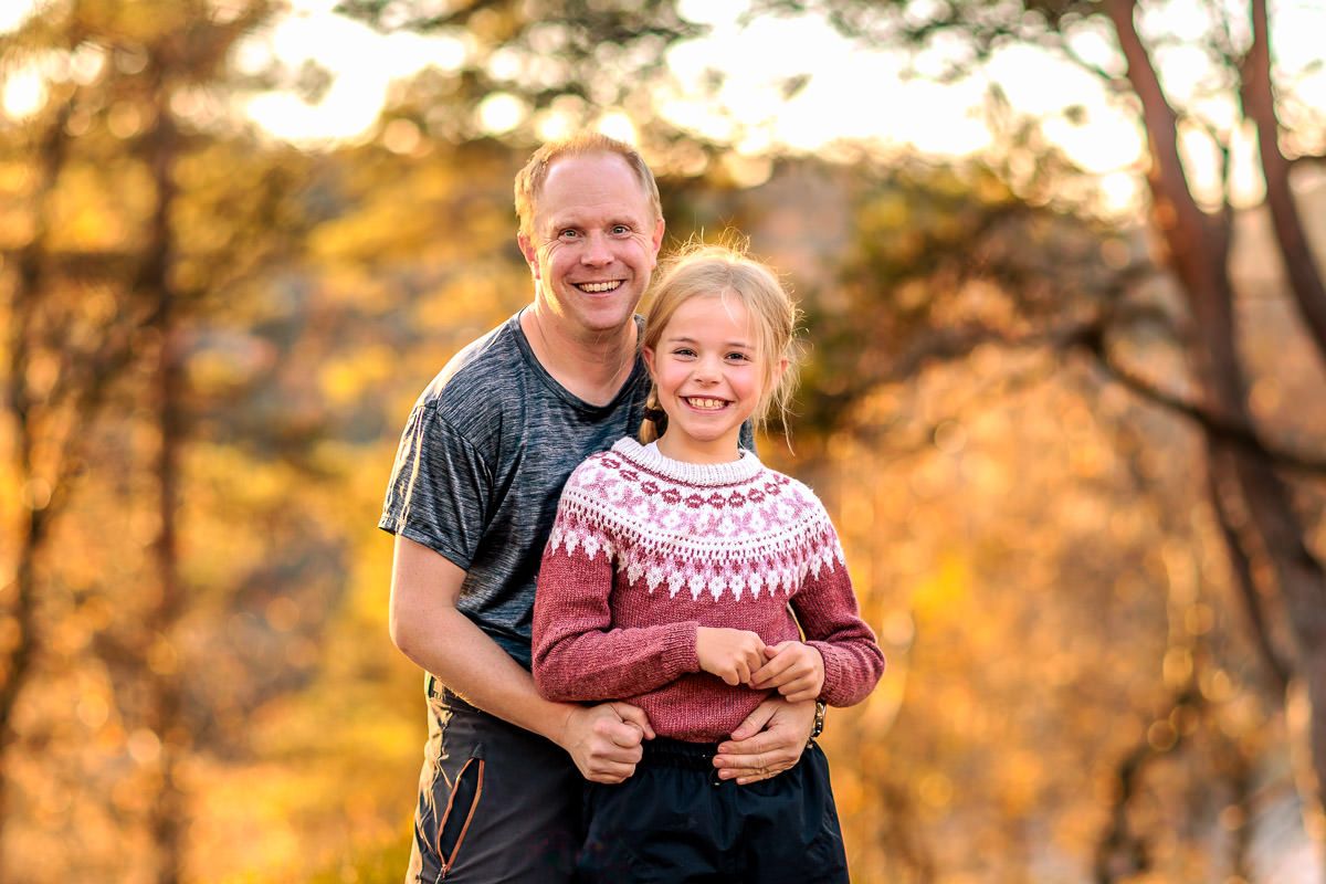 Far og datter står sammen i solnedgangen i en skog i klare høstfarger. Tatt av Ørstavik Foto.