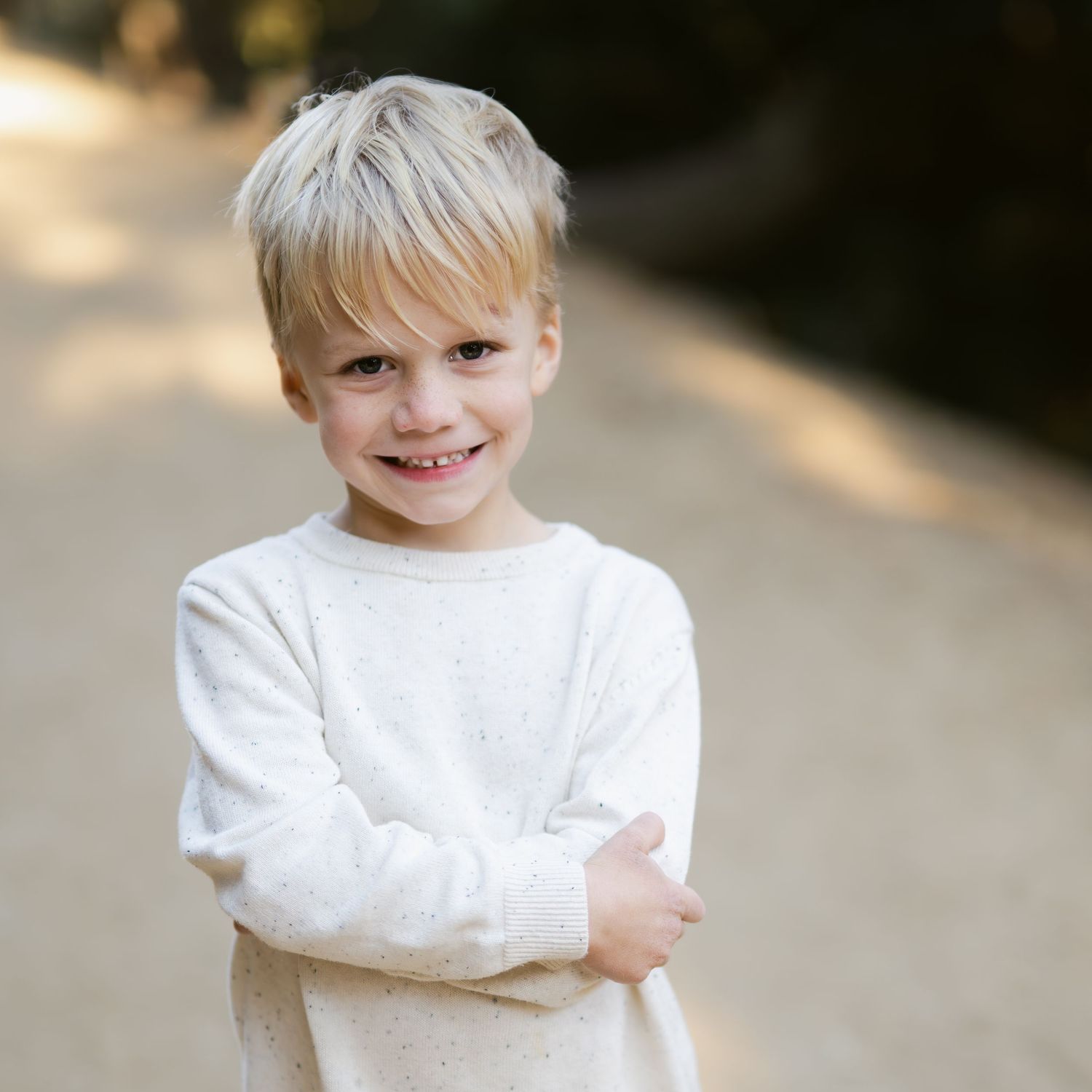 Child in white sweater showing various happy expressions in outdoor portrait series.