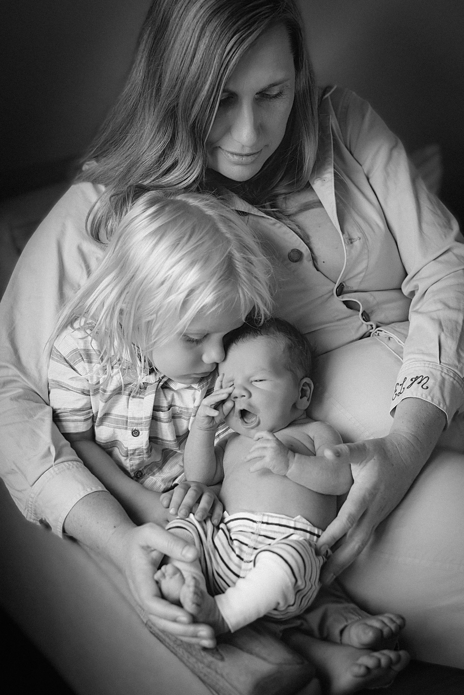 Black and white photo of tender family moment with newborn baby and sibling.