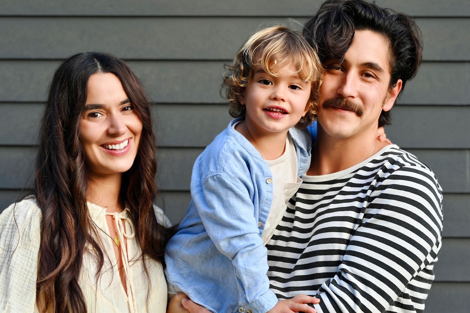 Happy family portrait outdoors against grey wall background.