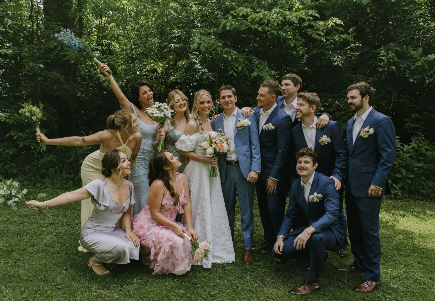 Wedding party strikes fun poses for a group photo in a natural outdoor setting.