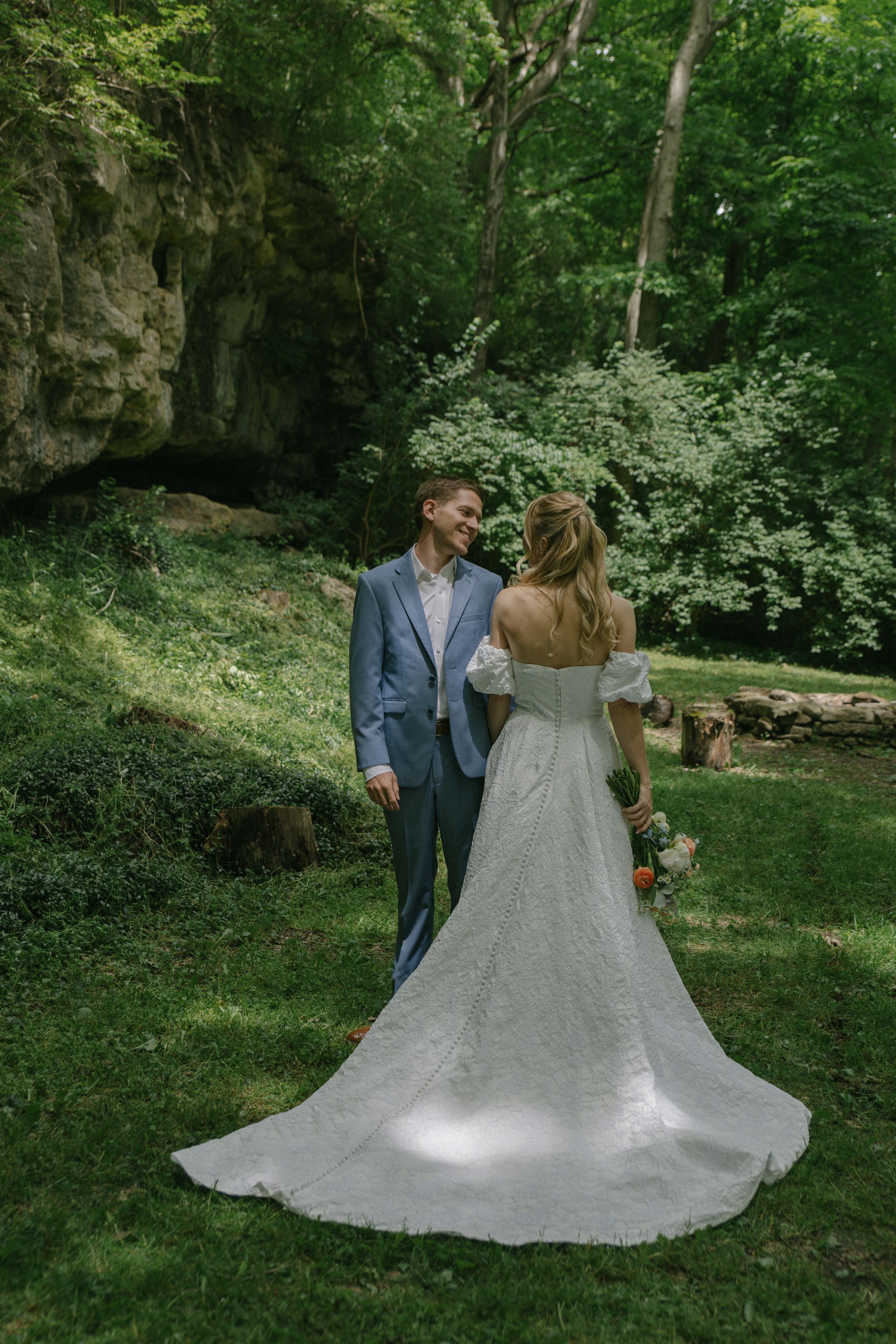 Elegant wedding couple posing in a serene woodland setting with flowing white dress.