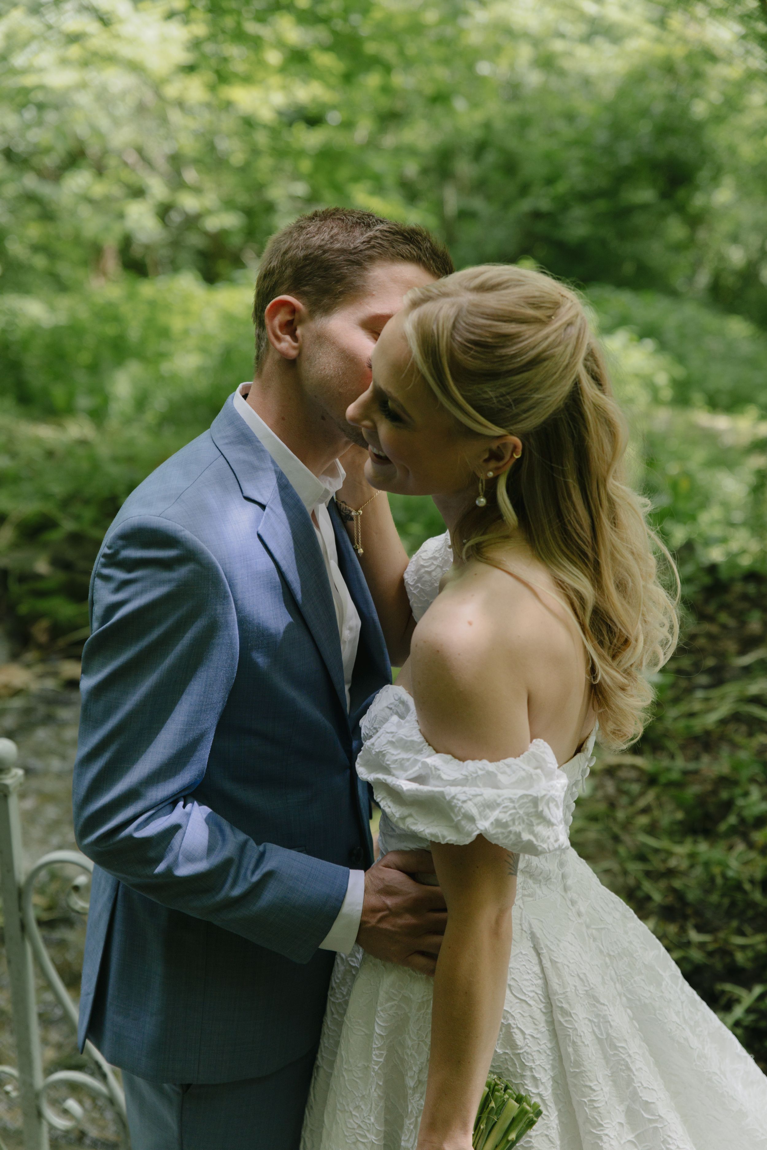 A romantic wedding moment captured in a lush green forest setting with the couple sharing an intimate embrace.