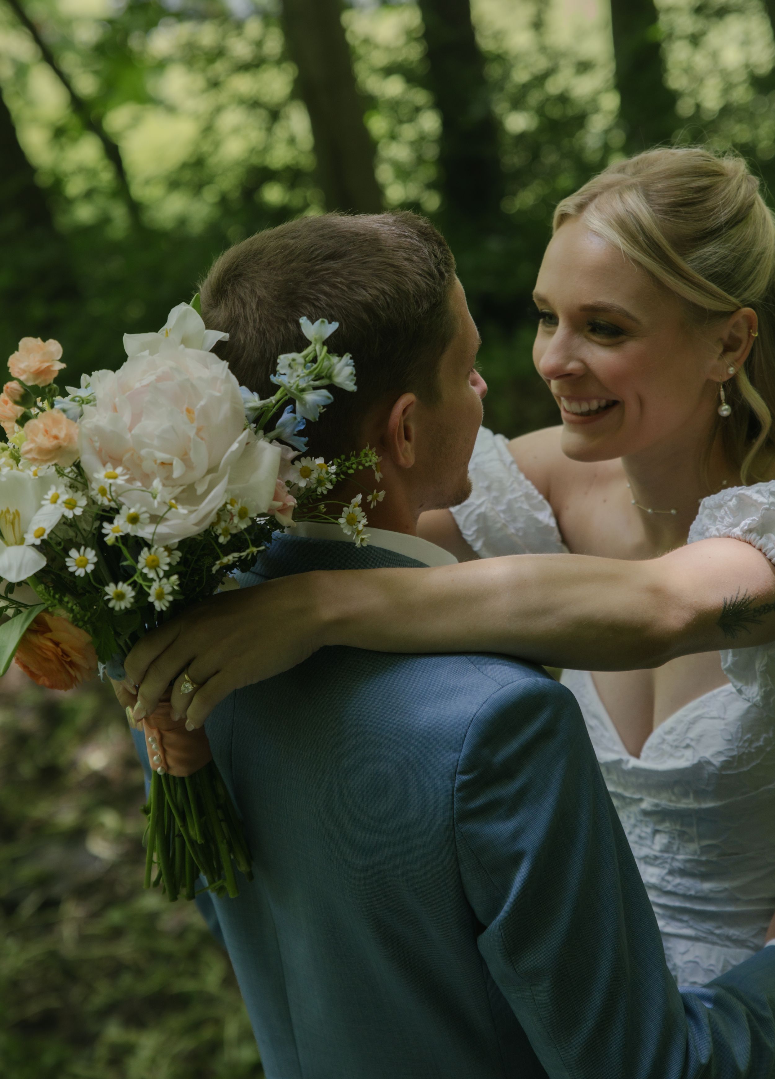 A joyful wedding embrace captured outdoors with a beautiful floral bouquet.