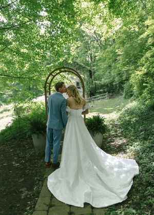 A full-length wedding photo showing a beautiful train dress under a garden arch.