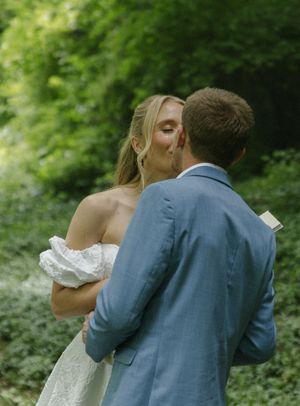 A tender wedding moment photographed in a sunlit forest clearing.