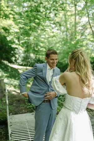 A romantic wedding moment captured in a lush forest setting showing a couple in blue suit and white dress.