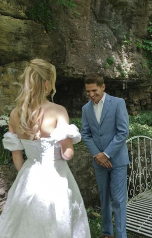 A wedding couple shares a moment near a stone wall backdrop with a decorative bench.