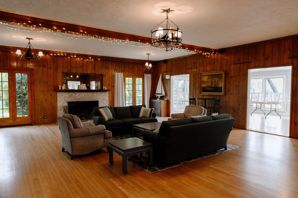 Spacious living room with wood paneling, hardwood floors, black leather sectional and chandelier lighting.