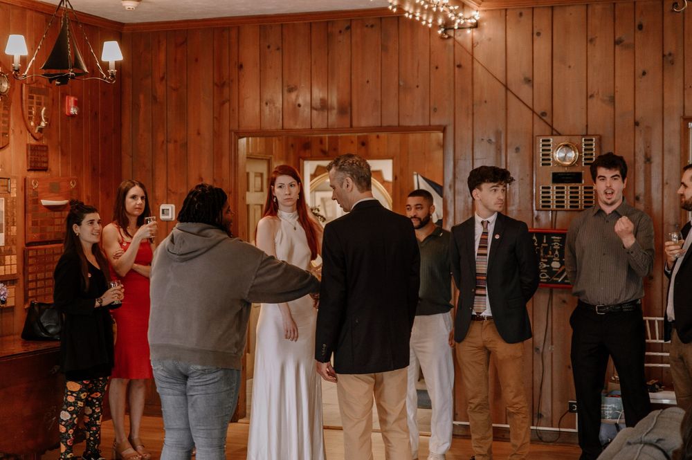 Wedding guests gather in a rustic wood-paneled reception hall during a celebration.