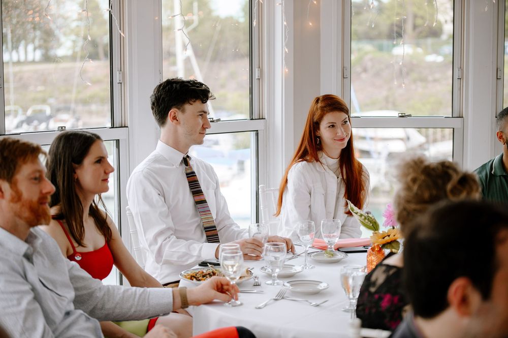 Group of friends enjoy casual dining and conversation at a sunny restaurant table near a large window.