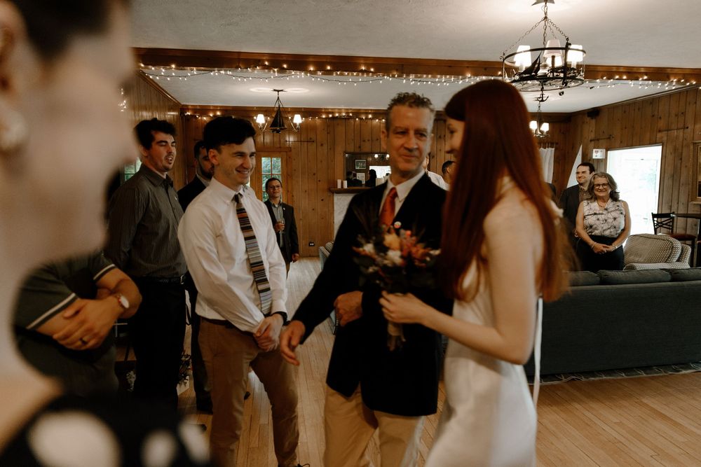 A group of guests mingling at an indoor celebration with string lights decorating the wood-paneled venue.