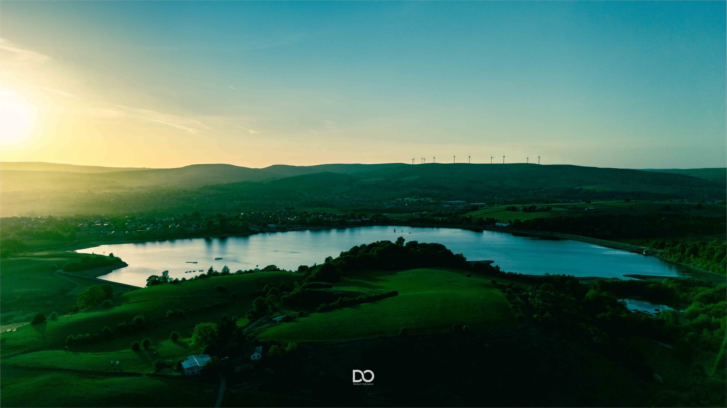 A scenic panoramic landscape view of rolling hills and a tranquil lake at sunset with a blue-tinted sky.