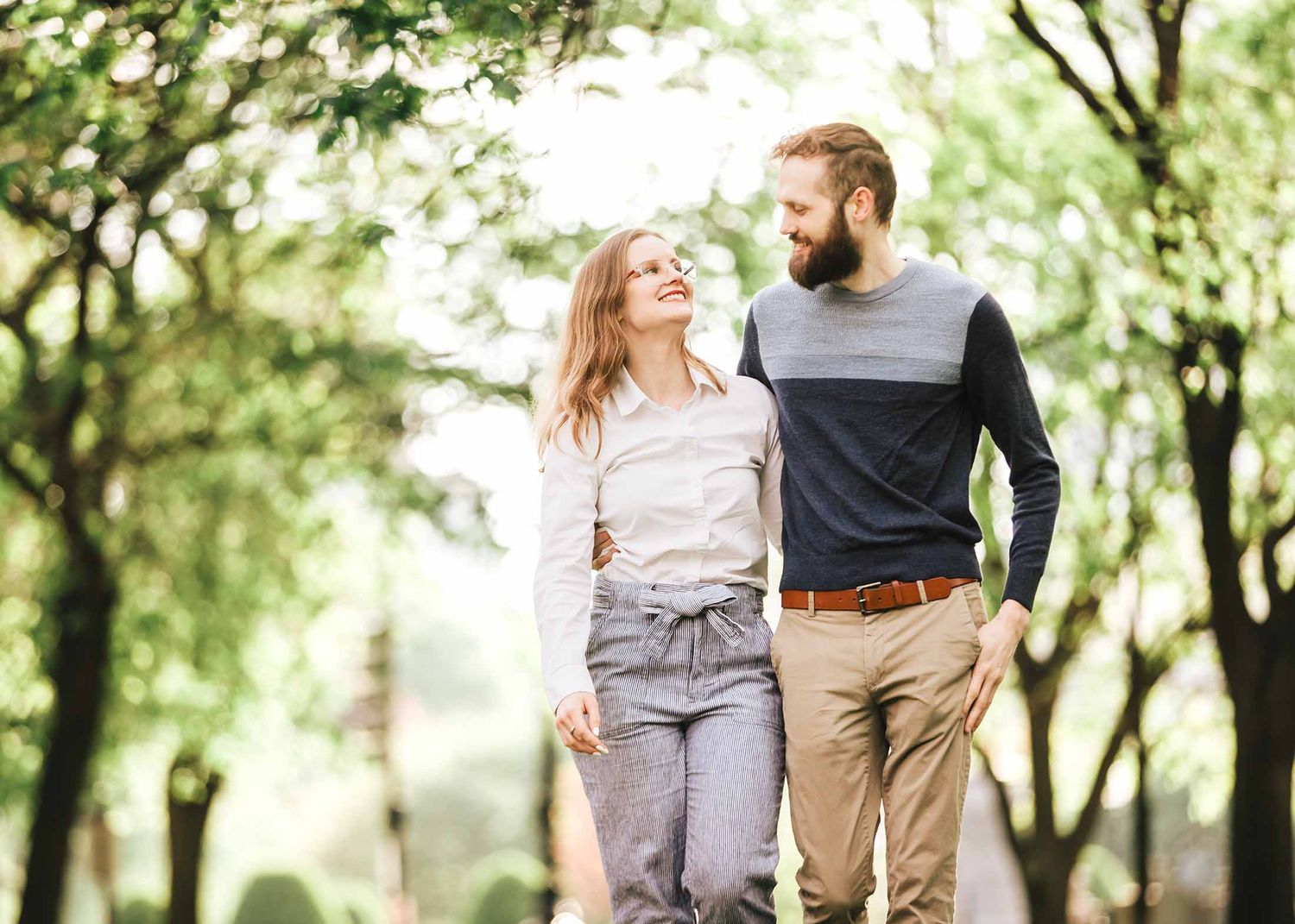 Engaged couple walking arm in arm under tree-lined Commonwealth Avenue Mall during early morning Boston engagement session
