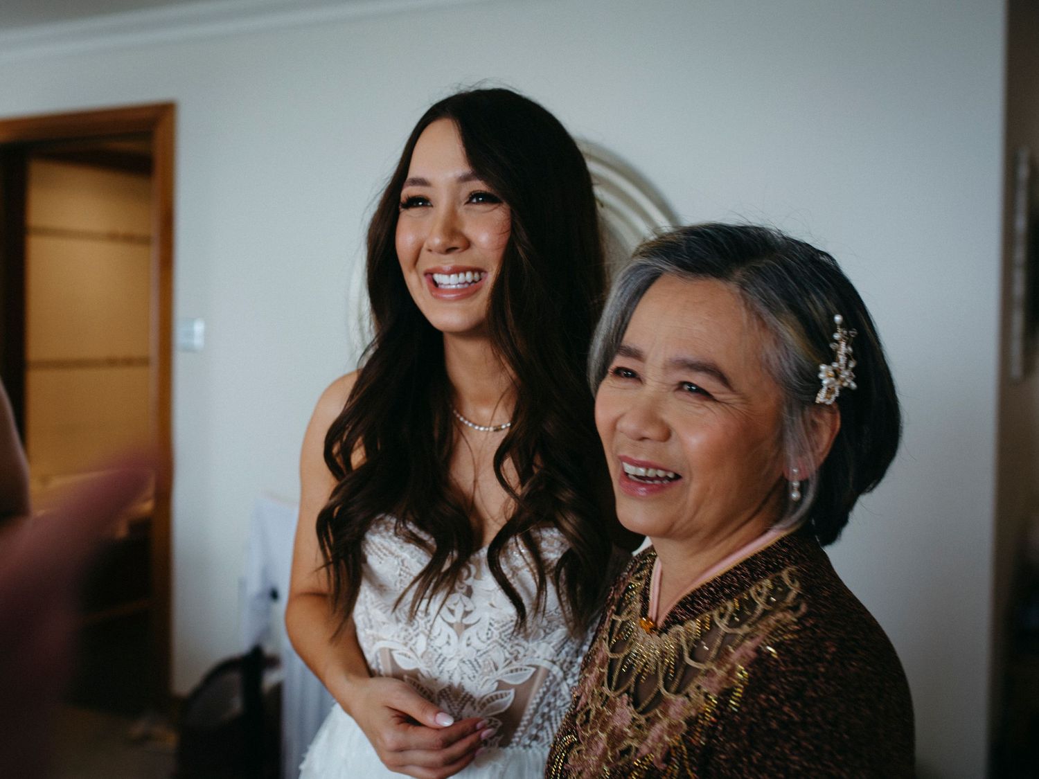 Two people sharing a joyful moment together, one wearing a white wedding dress and the other in embroidered formal attire.