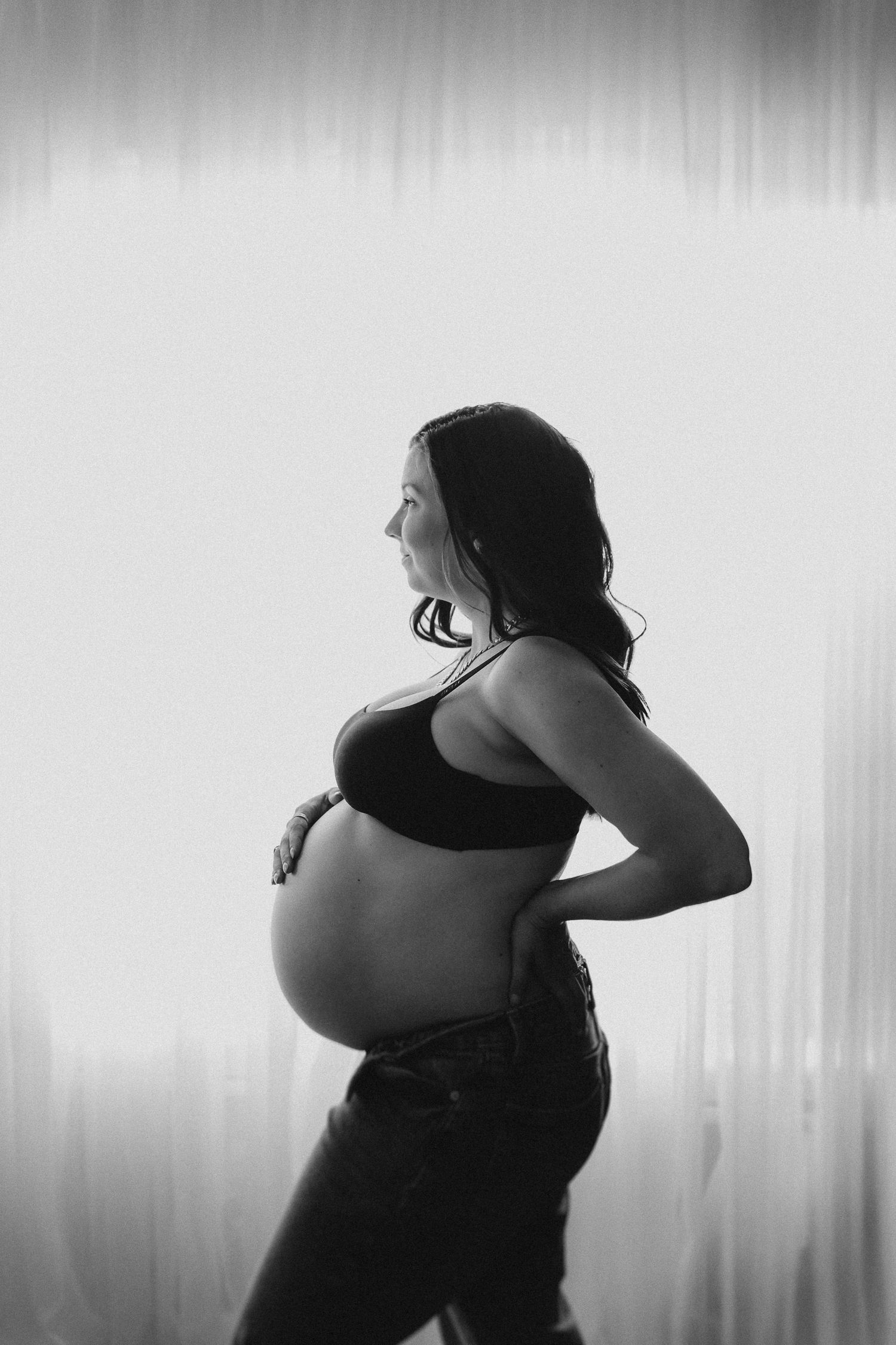 Black and white side profile portrait of pregnant woman in athletic wear against light backdrop.