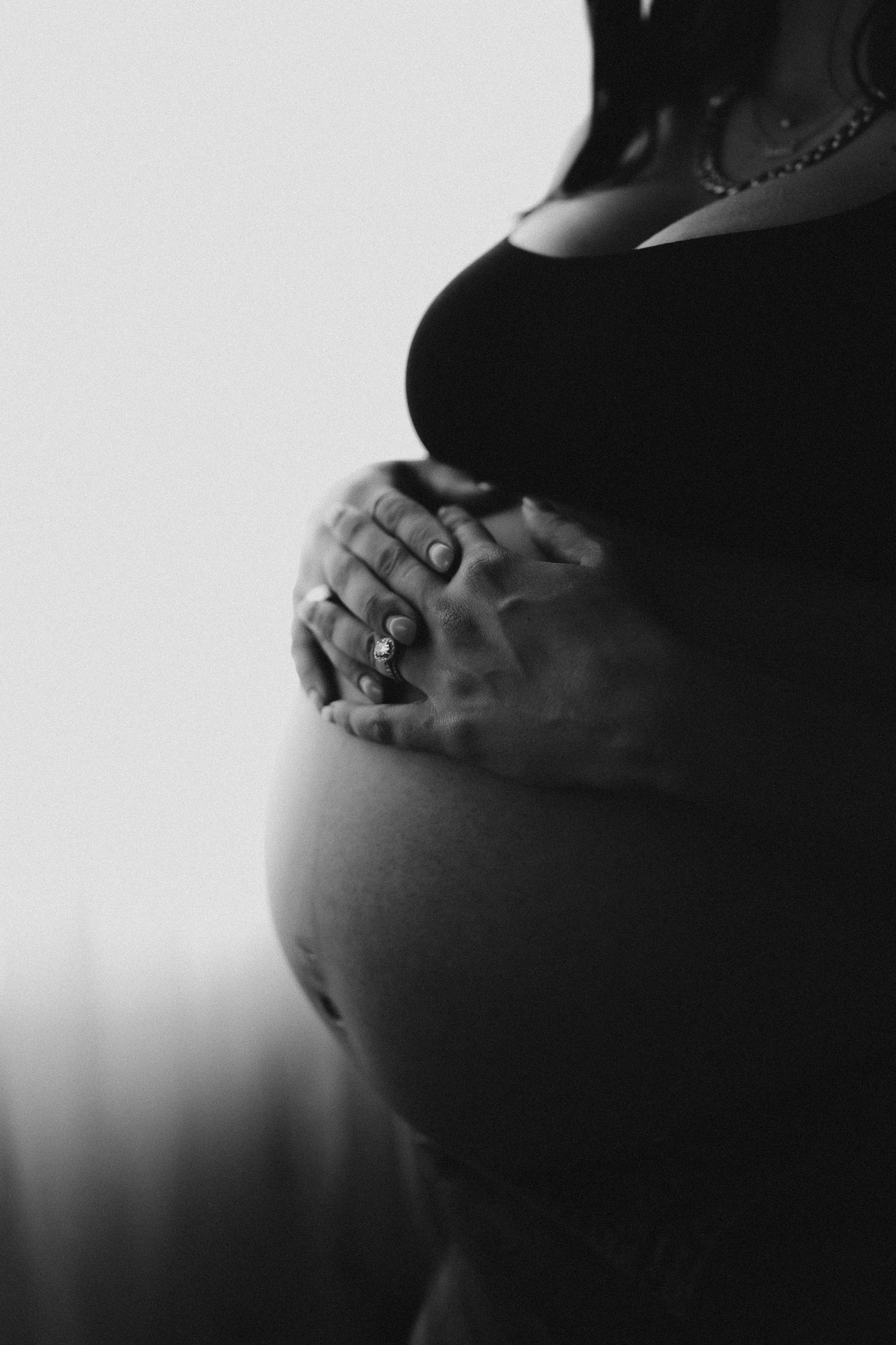 Black and white artistic photograph of a pregnant belly with hands gently resting on the round bump.