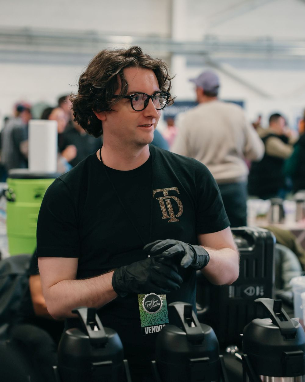 Person wearing black t-shirt and gloves operates equipment in an indoor facility during a training session.