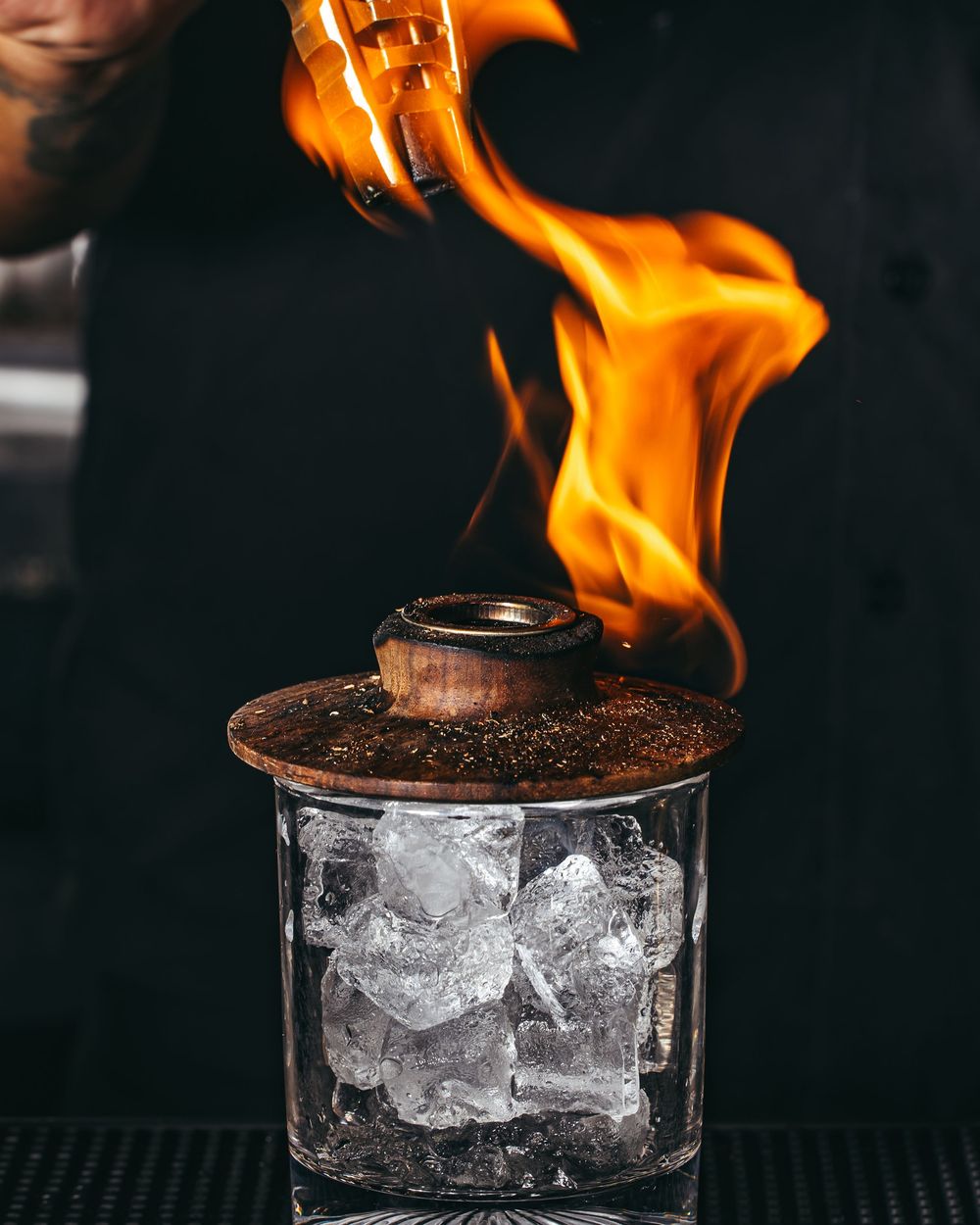 Orange flames dance atop a glass filled with ice cubes creating a dramatic fire and ice cocktail effect.