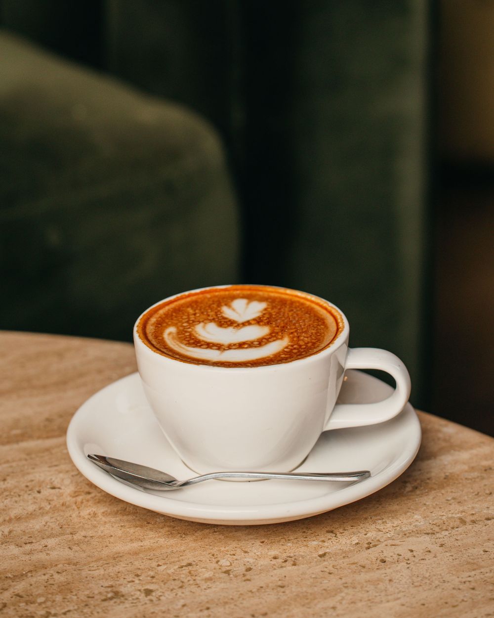 A sequence of four white coffee cups with latte art designs shown from different angles on a textured stone surface.