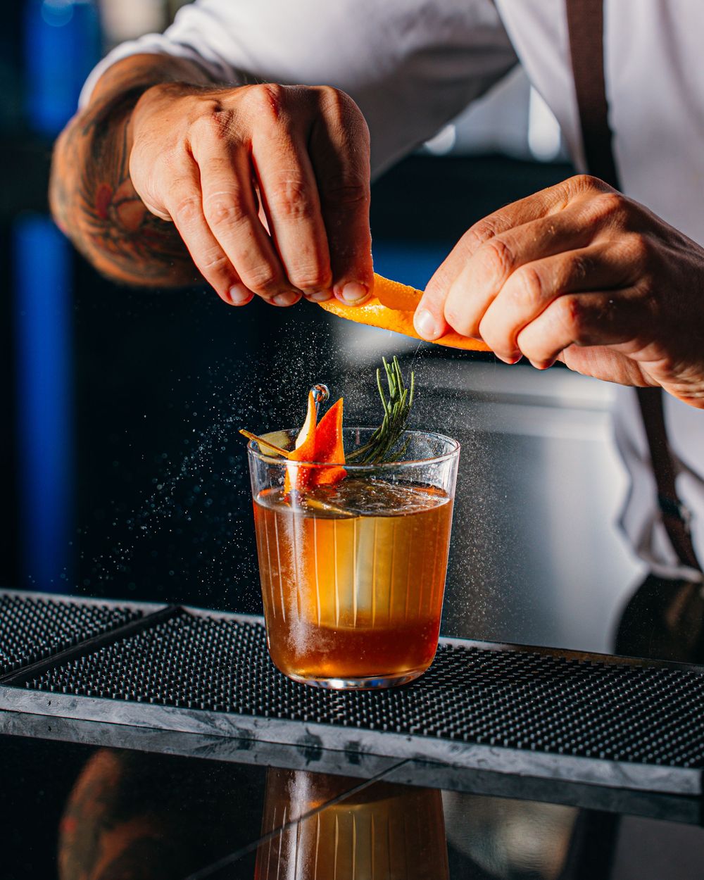 Bartender garnishing an orange cocktail with fresh citrus peel at a dark bar counter.