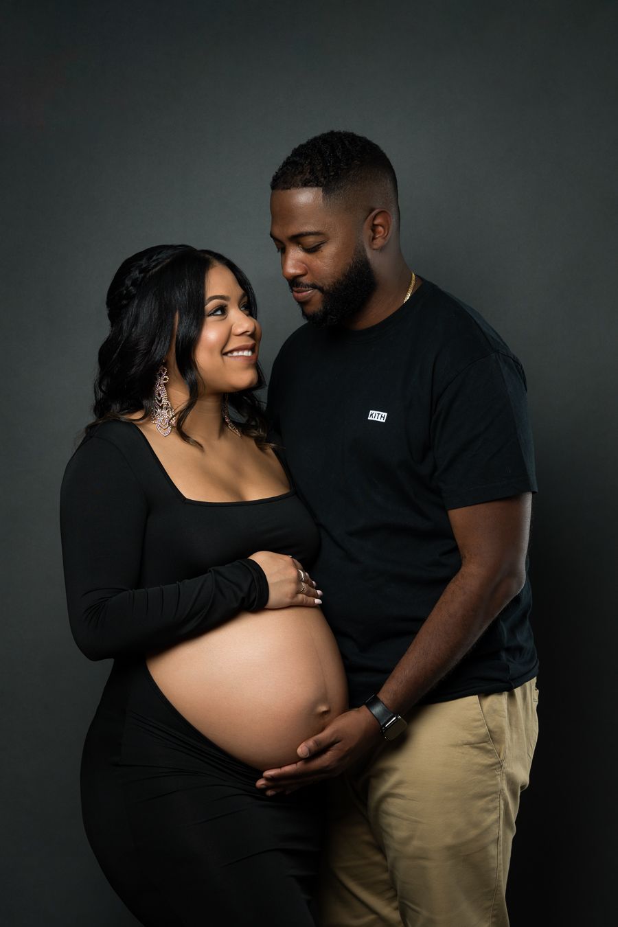 Intimate maternity photo featuring couple in black outfits against dark background with gentle lighting.