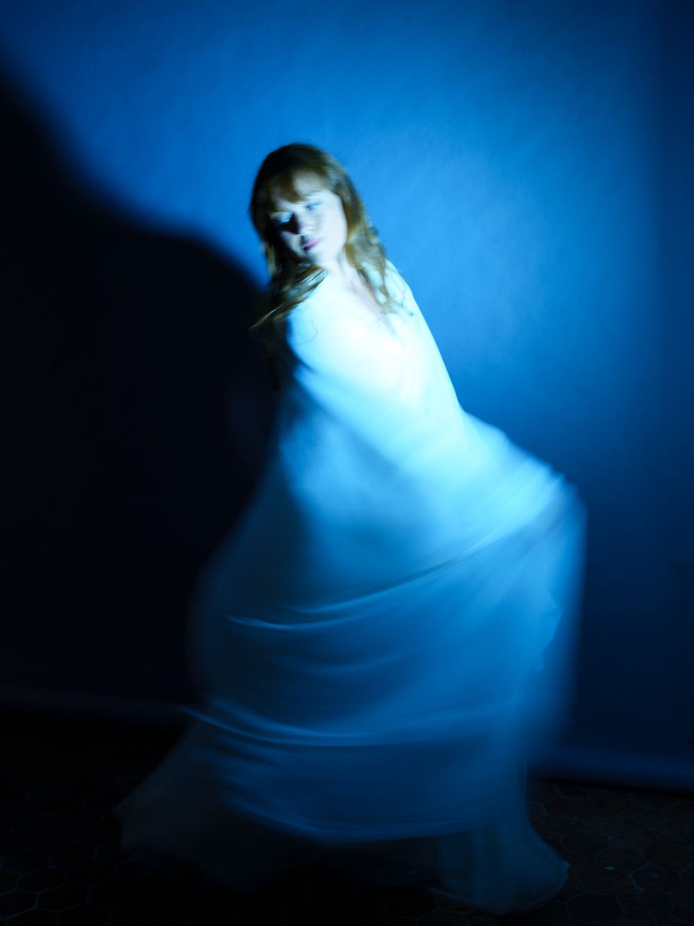 A woman in a flowing white dress spins gracefully against a blue background, captured with motion blur.