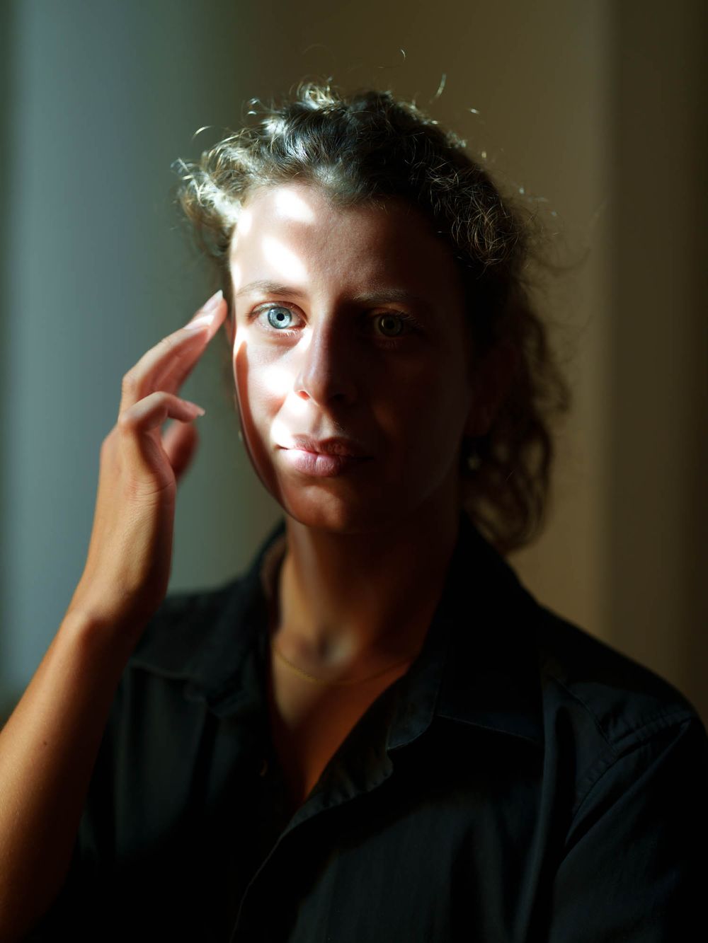 A woman with curly dark hair touches her temple, lit dramatically in a portrait-style photo.