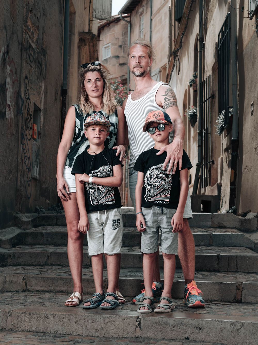 Family of four posing on stone steps in a rustic European alleyway, wearing matching graphic tees.