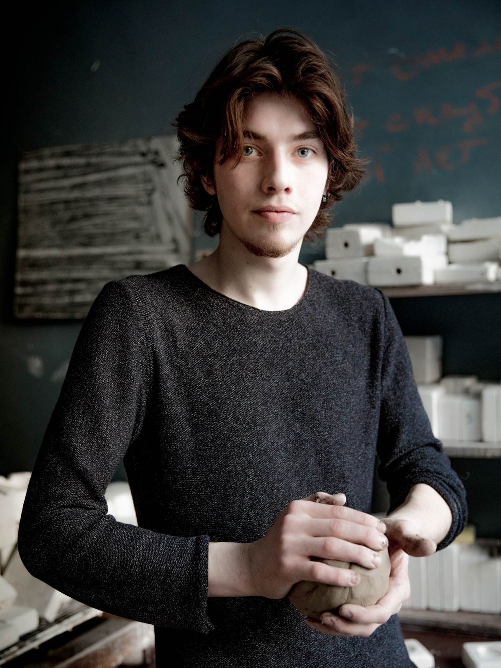 Young man in dark sweater holding clay pottery in an art studio workshop.