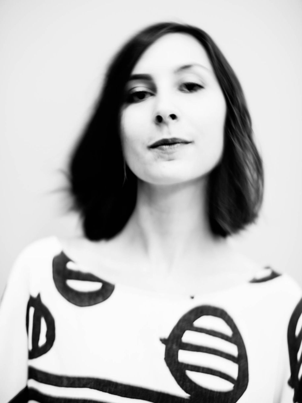 Black and white portrait of a woman with dark bob hair wearing a graphic print top with bold circular designs.