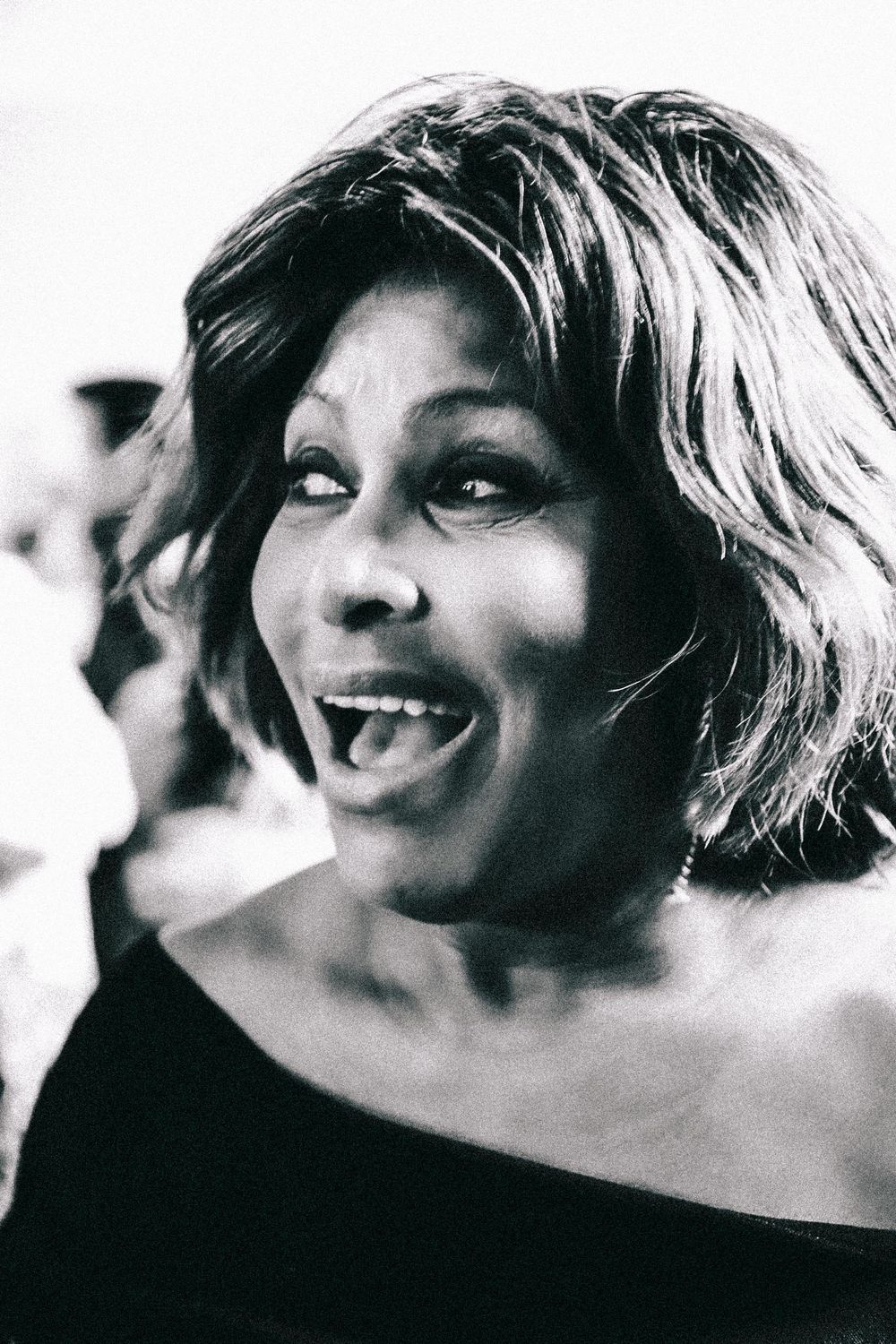 Black and white portrait showing an energetic expression with bright smile and tousled hair against blurred background.