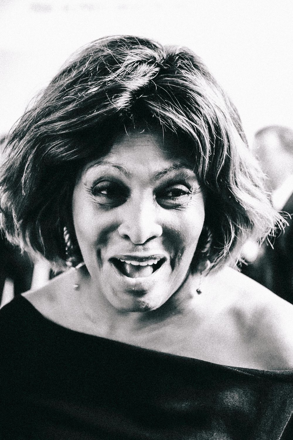 Black and white portrait photograph of a woman with short dark hair wearing an off-shoulder dress and expressing joy.
