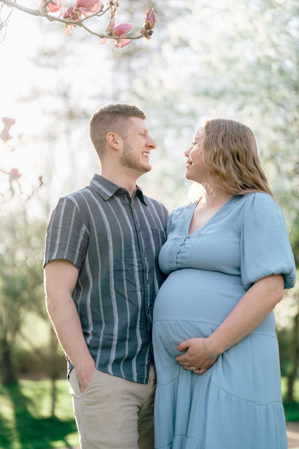 Expectant couple sharing a joyful moment outdoors with pink spring blossoms at a F.A. Seiberling Nature Realm in Akron, OH Maternity Session