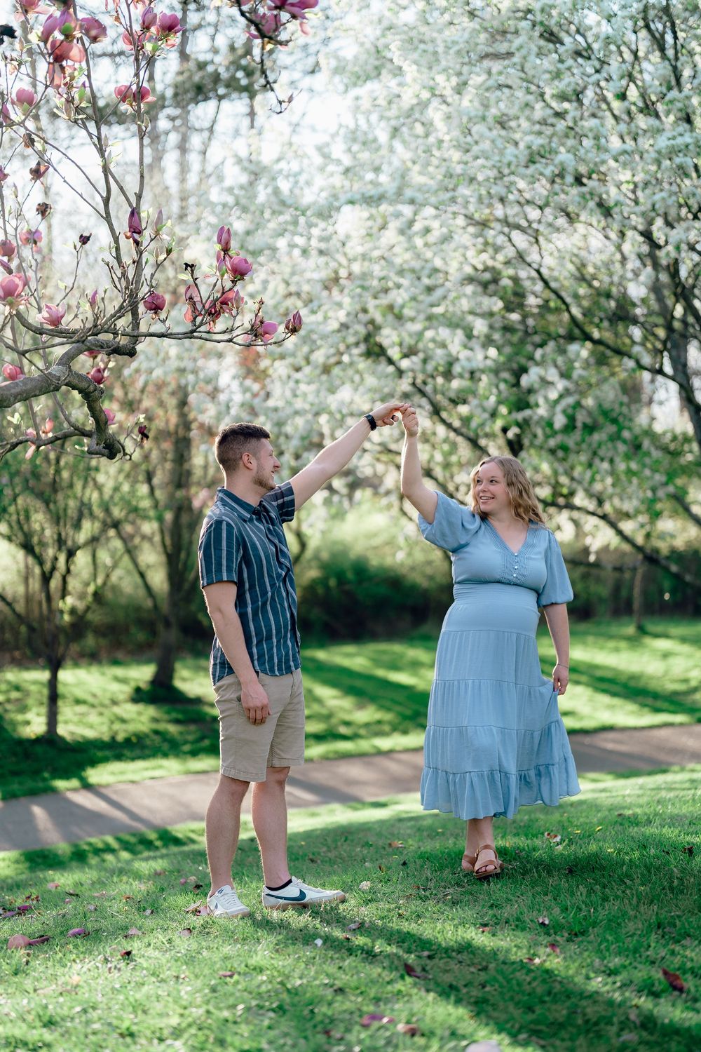 A couple dances joyfully together under flowering trees in a springtime garden at a Maternity session at F.A. Seiberling Nature Realm, OHIO